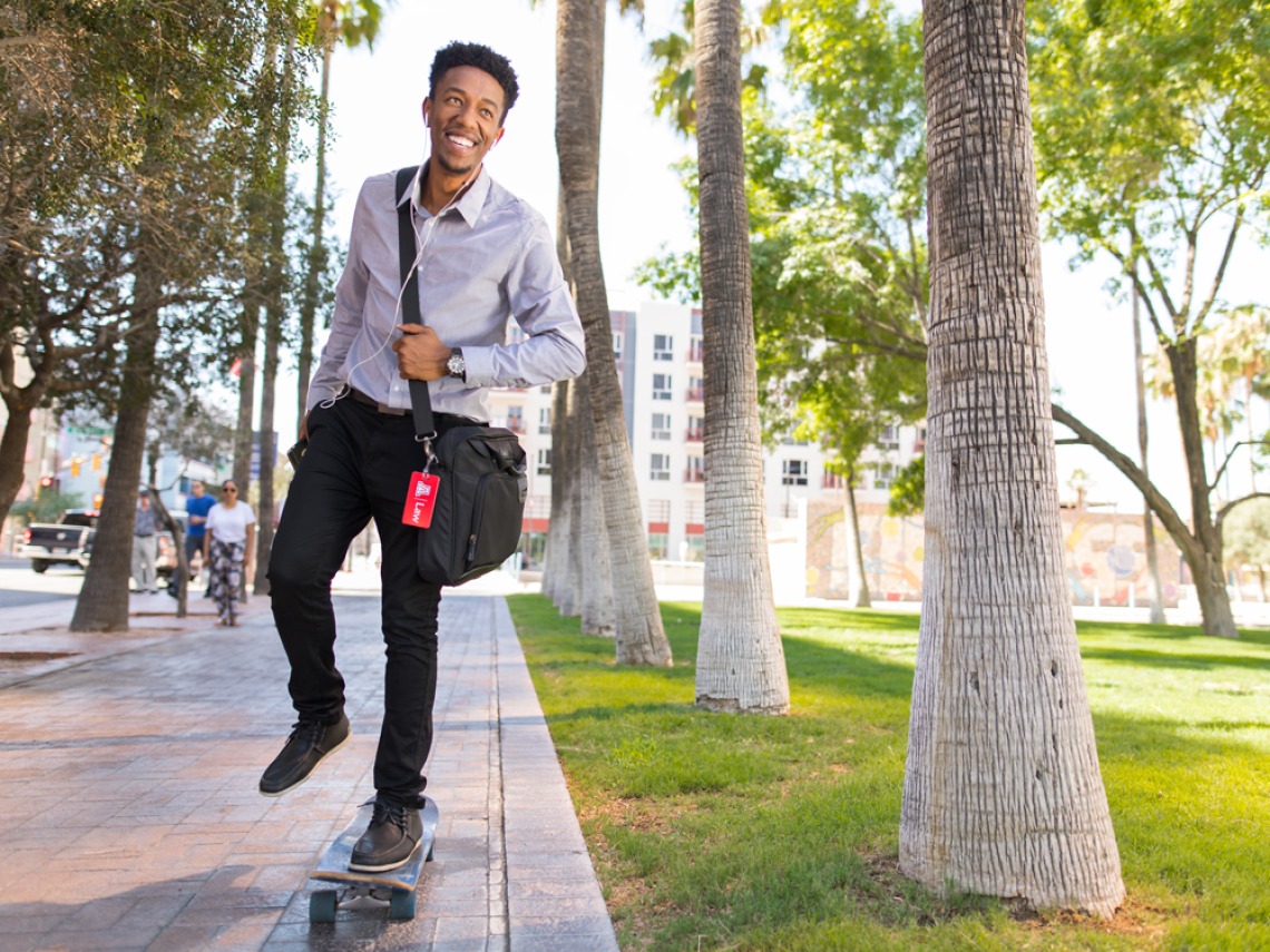 University of Arizona Law student smiling and riding a skateboard downtown